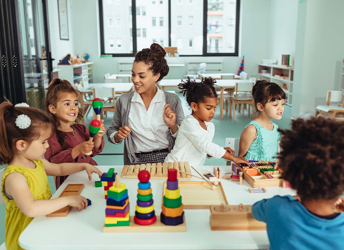 Child Care Center Insurance - Day Care Employee or Kindergarten Teacher Playing with Young Children in the Classroom and Creating Artwork and Building Blocks Together